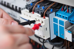 Closeup of male electrician examining fusebox with multimeter probe